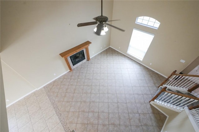 unfurnished living room featuring a high ceiling, a ceiling fan, baseboards, tile patterned floors, and a glass covered fireplace