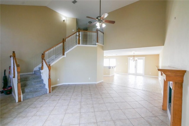 unfurnished living room with a fireplace, light tile patterned floors, ceiling fan with notable chandelier, baseboards, and stairs