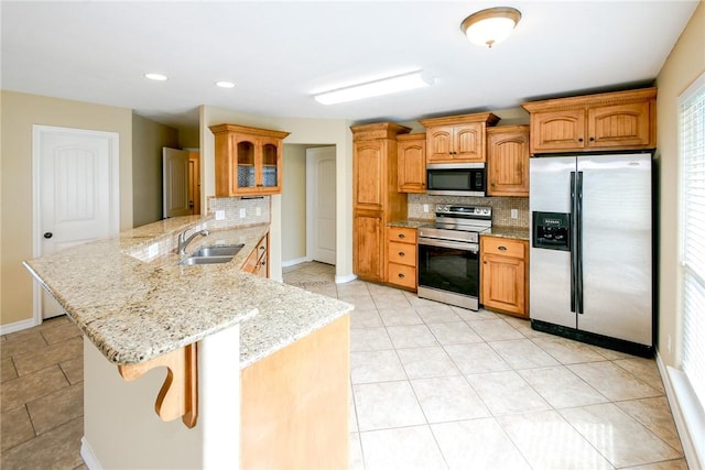 kitchen featuring light stone counters, a peninsula, a breakfast bar, a sink, and appliances with stainless steel finishes