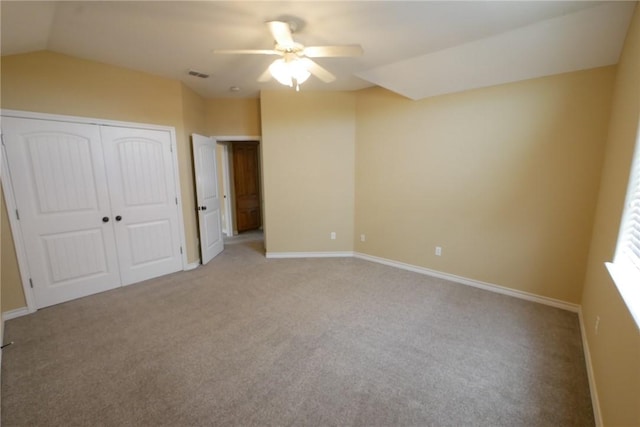 unfurnished bedroom with lofted ceiling, light carpet, visible vents, baseboards, and a closet