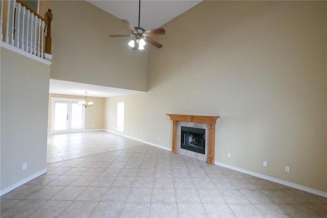 unfurnished living room with light tile patterned flooring, baseboards, a tiled fireplace, and ceiling fan with notable chandelier