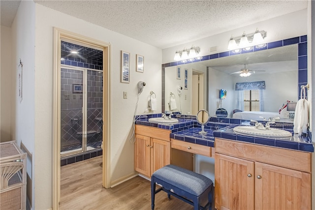 bathroom featuring a textured ceiling, hardwood / wood-style flooring, vanity, ceiling fan, and a shower with shower door