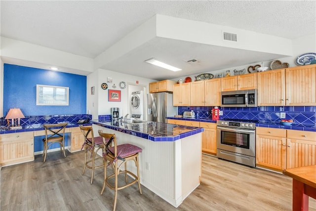 kitchen featuring appliances with stainless steel finishes, estacked washer and dryer, a breakfast bar, light brown cabinets, and decorative backsplash