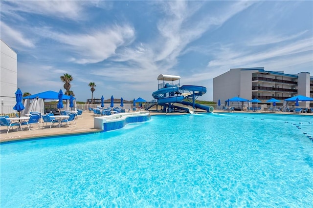 community pool with a water slide, a patio, and fence