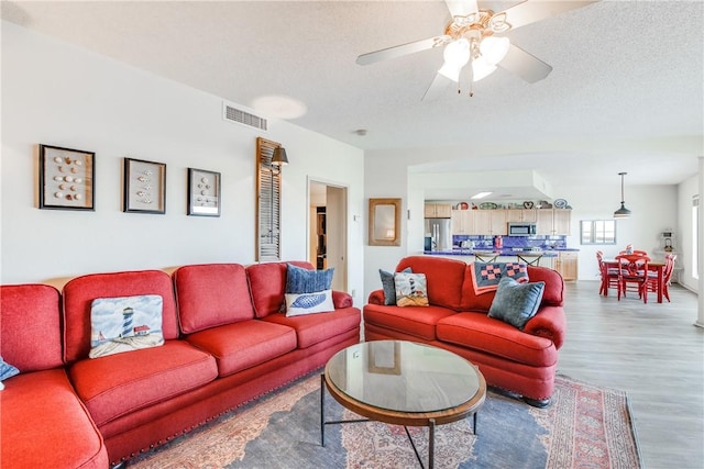 living room with wood finished floors, a ceiling fan, and a textured ceiling