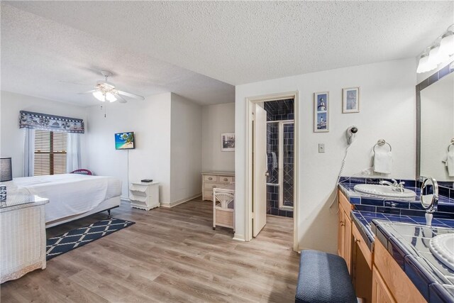 bedroom featuring a textured ceiling, light wood-type flooring, a sink, a ceiling fan, and baseboards