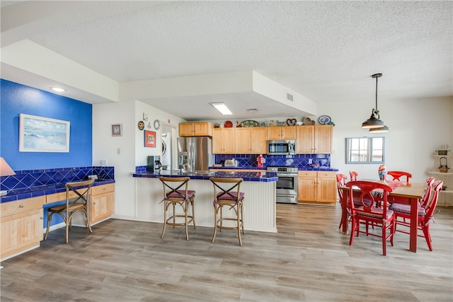 kitchen featuring stainless steel appliances, backsplash, a kitchen bar, light hardwood / wood-style floors, and kitchen peninsula