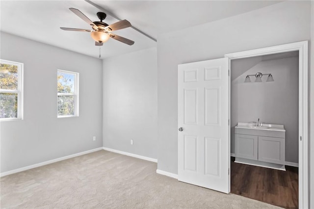 unfurnished bedroom featuring ceiling fan, sink, light carpet, and ensuite bath