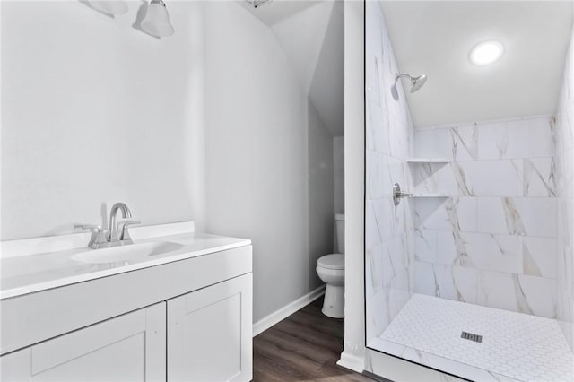 bathroom featuring vanity, vaulted ceiling, tiled shower, hardwood / wood-style flooring, and toilet