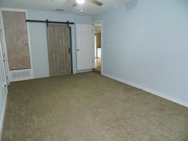 unfurnished bedroom featuring ceiling fan, a barn door, and carpet