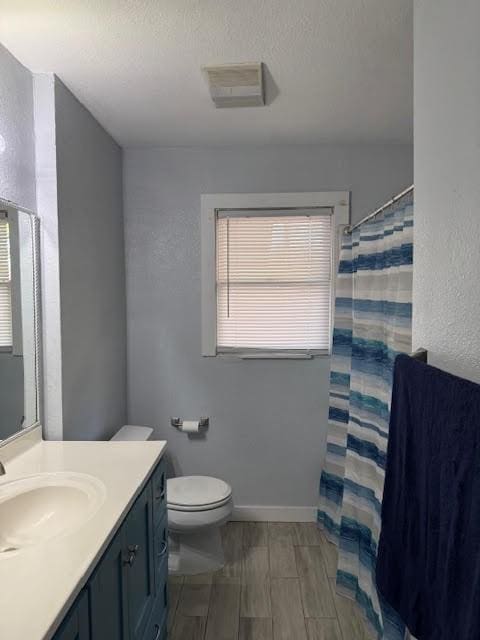 bathroom with toilet, vanity, a healthy amount of sunlight, and walk in shower