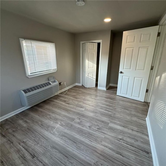 unfurnished bedroom featuring light wood-style flooring, baseboards, a closet, and a wall mounted air conditioner