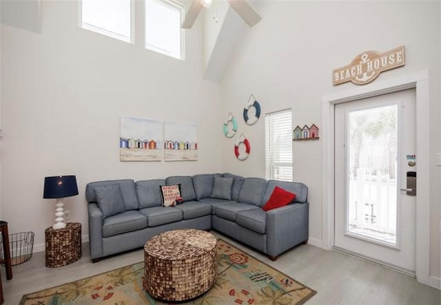 living room featuring ceiling fan, a high ceiling, and light wood-type flooring