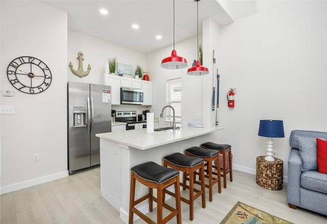 kitchen featuring kitchen peninsula, hanging light fixtures, appliances with stainless steel finishes, white cabinetry, and a breakfast bar