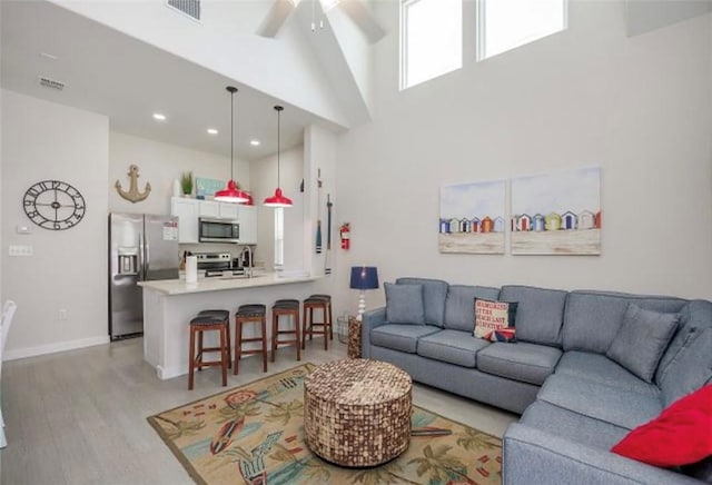 living room with ceiling fan, light hardwood / wood-style floors, and a high ceiling