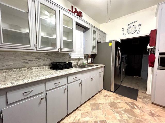 kitchen featuring stainless steel fridge with ice dispenser, gray cabinets, light stone countertops, decorative backsplash, and sink