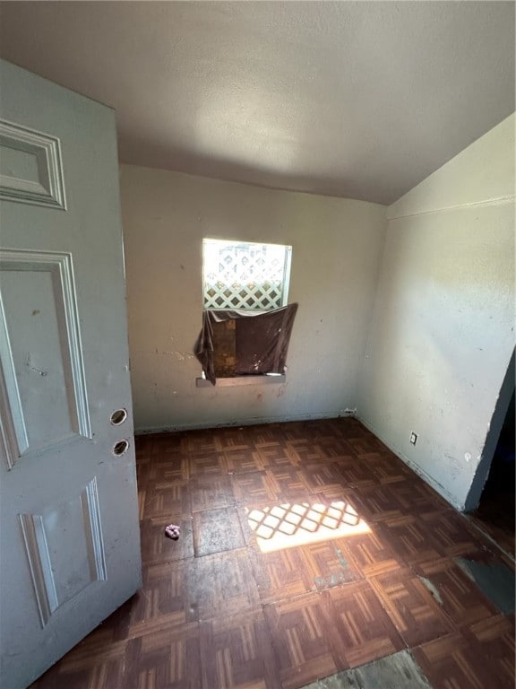 empty room with vaulted ceiling and dark parquet flooring