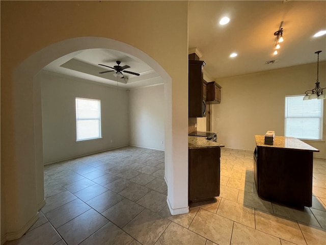 interior space featuring light stone counters, crown molding, dark brown cabinetry, a raised ceiling, and ceiling fan with notable chandelier