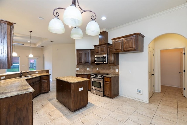 kitchen with arched walkways, stainless steel appliances, a sink, hanging light fixtures, and tasteful backsplash