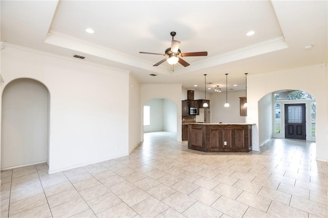 interior space with visible vents, arched walkways, a ceiling fan, ornamental molding, and a tray ceiling