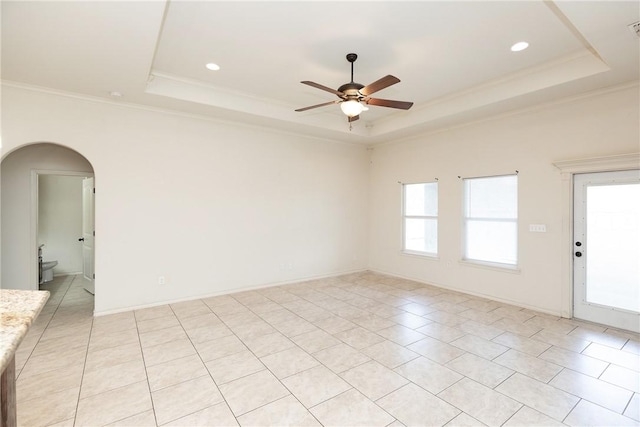 empty room featuring arched walkways, a tray ceiling, ornamental molding, and a ceiling fan