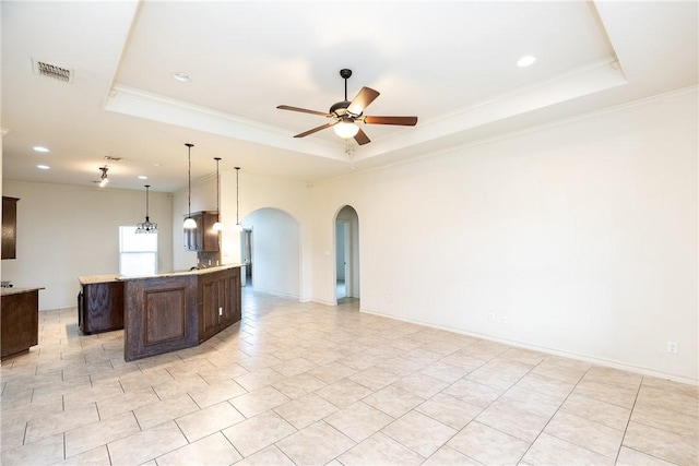 kitchen with arched walkways, dark brown cabinetry, visible vents, open floor plan, and a tray ceiling