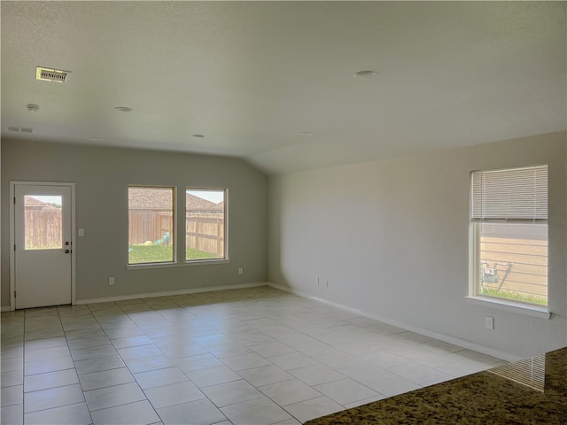 empty room featuring lofted ceiling, a healthy amount of sunlight, and light tile patterned floors