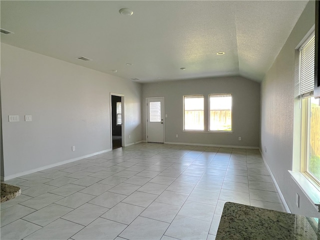 tiled empty room with lofted ceiling, a textured ceiling, and plenty of natural light