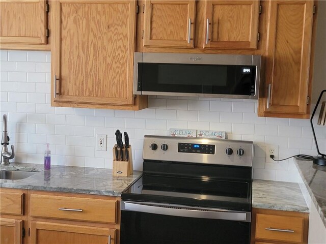 kitchen with a sink, light stone countertops, tasteful backsplash, and stainless steel appliances