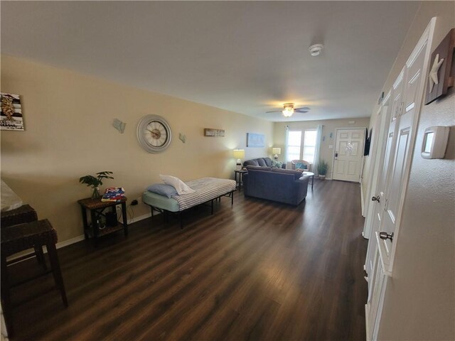 living room with baseboards, a ceiling fan, and dark wood-style flooring