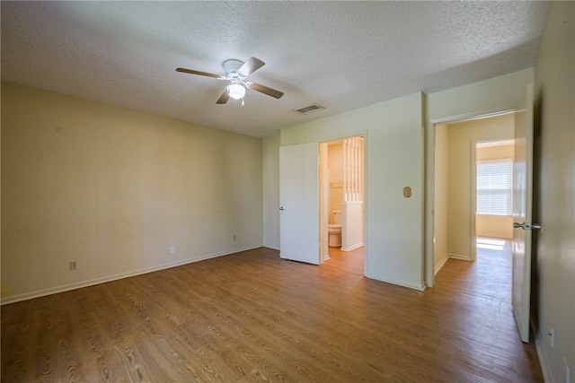 unfurnished bedroom with ceiling fan, ensuite bathroom, light wood-type flooring, and a textured ceiling