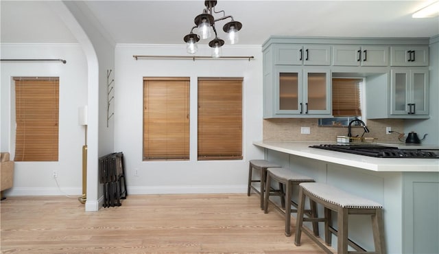 kitchen with a kitchen bar, light countertops, backsplash, light wood-style floors, and glass insert cabinets