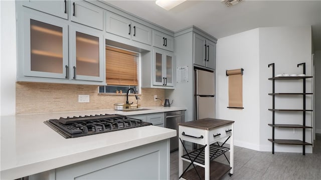 kitchen with light countertops, stainless steel appliances, tasteful backsplash, glass insert cabinets, and gray cabinetry