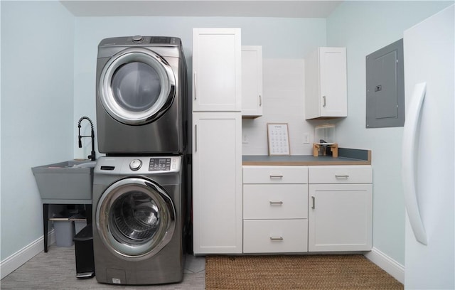 clothes washing area featuring stacked washer and dryer, cabinet space, baseboards, and electric panel