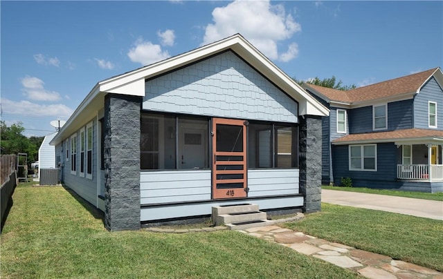 view of front of home featuring a front lawn, central air condition unit, a sunroom, and fence