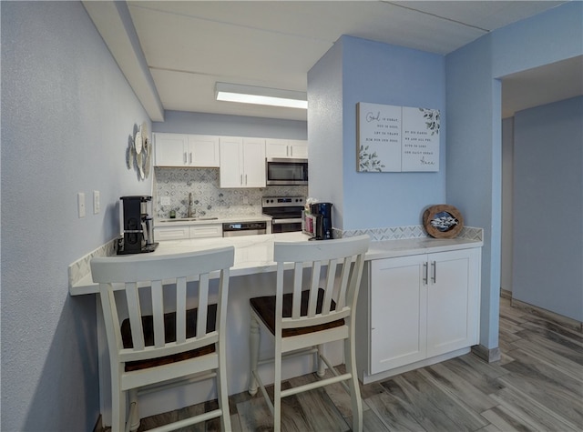 kitchen with stainless steel appliances, decorative backsplash, sink, white cabinetry, and light hardwood / wood-style flooring