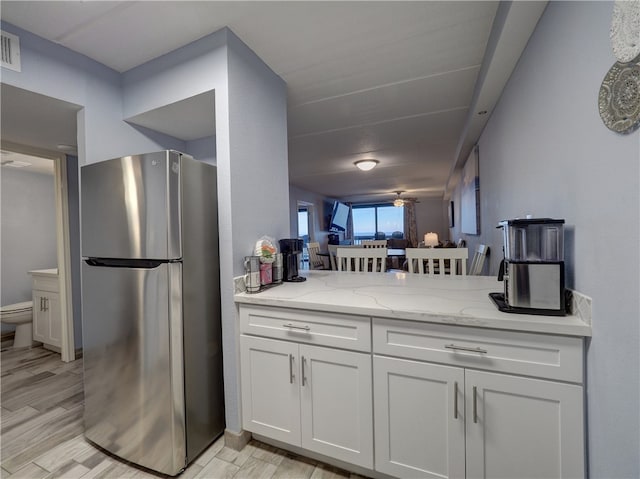 kitchen featuring white cabinetry, light wood-type flooring, stainless steel refrigerator, light stone countertops, and ceiling fan