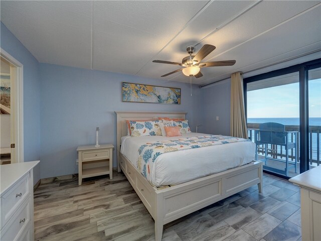 bedroom featuring access to outside, light hardwood / wood-style floors, a water view, and ceiling fan