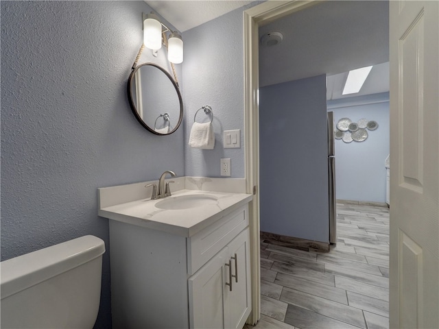 bathroom featuring toilet, vanity, a skylight, and hardwood / wood-style floors