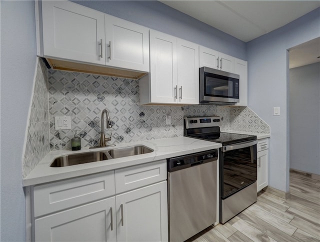 kitchen with backsplash, appliances with stainless steel finishes, sink, light hardwood / wood-style floors, and white cabinets