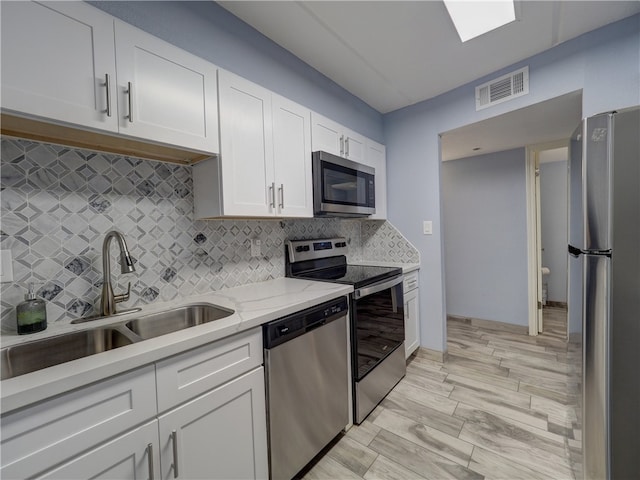 kitchen featuring stainless steel appliances, white cabinetry, backsplash, light stone countertops, and sink