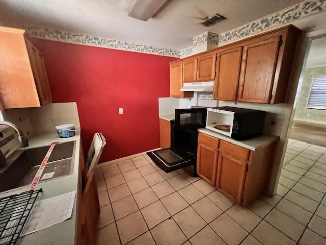667 Lisa Ann Dr, Aransas Pass, TX 78336 - kitchen with light countertops, under cabinet range hood, light tile patterned flooring, visible vents, and brown cabinets
