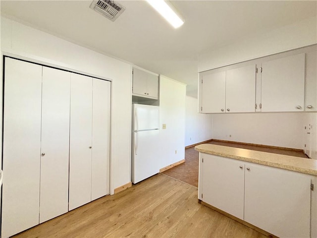 kitchen with light wood finished floors, light countertops, visible vents, freestanding refrigerator, and white cabinetry