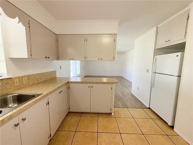 kitchen with light tile patterned floors, freestanding refrigerator, a peninsula, light countertops, and white cabinetry