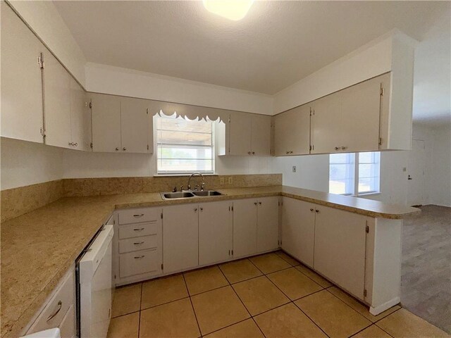 kitchen with light tile patterned floors, dishwasher, a peninsula, light countertops, and a sink