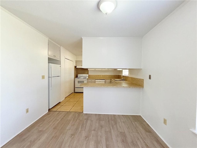 kitchen featuring light countertops, light wood-style flooring, a sink, white appliances, and a peninsula