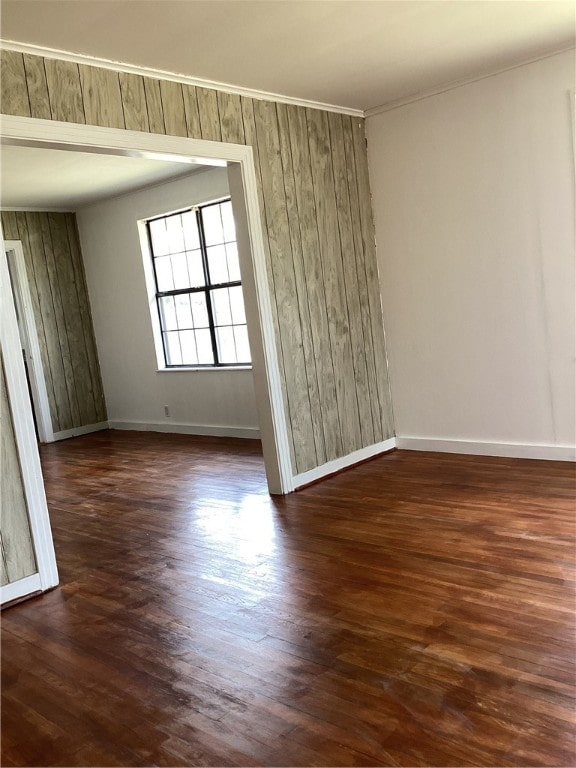 empty room with dark hardwood / wood-style flooring, wooden walls, and crown molding