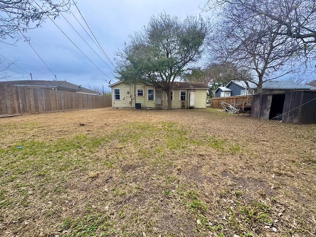 back of property featuring fence, a lawn, and an outbuilding