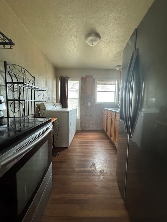 kitchen with dark wood-style flooring, black refrigerator with ice dispenser, brown cabinetry, washing machine and dryer, and stainless steel range with electric stovetop