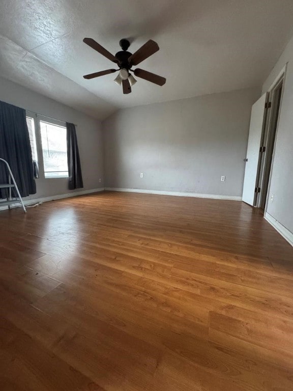 spare room with vaulted ceiling, wood finished floors, a ceiling fan, and baseboards